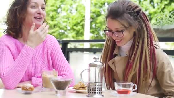 Duas jovens amigas estão almoçando juntas em um café ao ar livre durante um dia na primavera. — Vídeo de Stock