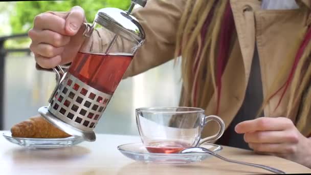 Close-up van vrouwelijke handen met een kopje fruitthee. Meisje met lange dreadlocks drinkt in een koffiehuis op straat — Stockvideo