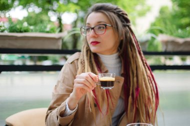 Uzun saçlı pozitif zeki kız bir kahve dükkanında şeffaf bir fincan espresso ile dinleniyor..