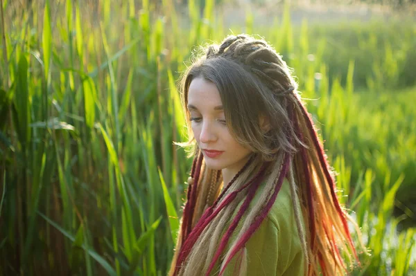 Buiten portret van een meisje met dreadlocks en groen shirt in een stadspark in de buurt van het meer tijdens een zonsondergang, wees vrij concept. — Stockfoto