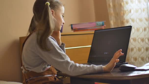 Bakåt syn på liten flicka med två hästsvansar säger hej för sin lärare med hjälp av videokamera på svart bärbar dator hemma på grund av självisolering på grund av Coronavirus Covid-19. Fjärrutbildning — Stockvideo