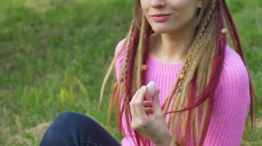 Örgü süveter ve uzun rastalı yetişkin bir kız, açık hava arka planında vumfit, imbuilding veya meditasyon için pembe kuvars yumurtası tutuyor.