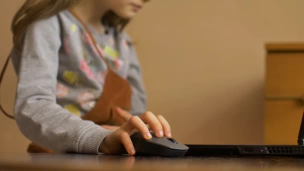 La mano de un niño pequeño sostiene un ratón de computadora en el fondo de la pantalla del ordenador portátil. Educación remota en línea durante la cuarentena y el autoaislamiento durante su estancia en casa — Vídeos de Stock