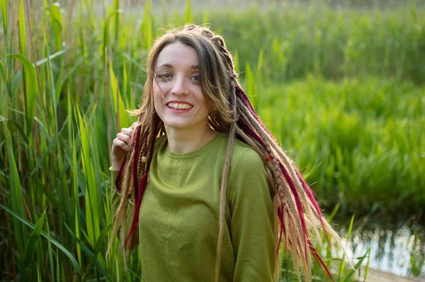 Buiten portret van een meisje met dreadlocks en groen shirt in een stadspark in de buurt van het meer tijdens een zonsondergang, wees vrij concept. — Stockfoto