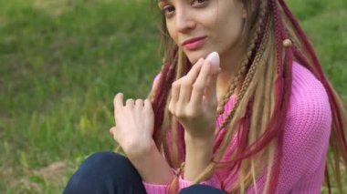 Örgü süveter ve uzun rastalı yetişkin bir kız, açık hava arka planında vumfit, imbuilding veya meditasyon için pembe kuvars yumurtası tutuyor.