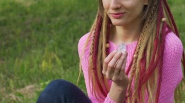Örgü kazaklı, uzun saçlı yetişkin bir kız vumfit için şeffaf menekşe ametist yoni yumurtası tutuyor. Açık havada vücut arka planında meditasyon yapıyor.
