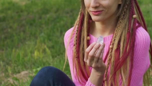 Vuxen flicka i stickad tröja med långa dreadlocks håller transparent violett ametist yoni ägg för vumfit, imbuilding eller meditation utomhus på hennes kropp bakgrund utomhus — Stockvideo