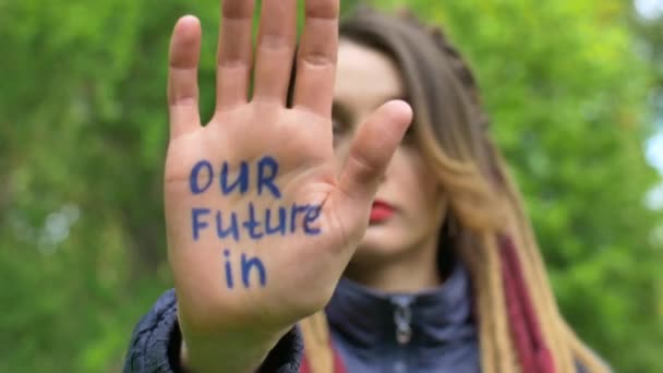 Moderne seriøs pige med lange dreadlocks viser hænder med skriftlig slogan Vores fremtid i dine hænder på grønt træ baggrund. Ansvar, begreber vedrørende klimaændringer – Stock-video