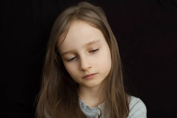Retrato de una niña triste con el pelo largo y rubio y los ojos cerrados sobre fondo negro en el estudio —  Fotos de Stock