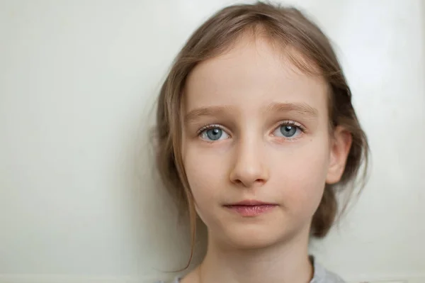 Retrato de uma menina com longos cabelos loiros e olhos azuis com rabo de cavalo está de pé sobre fundo branco em estúdio — Fotografia de Stock