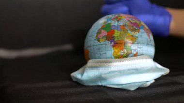 Üzerinde Ukrayna Kiril alfabesiyle yazılmış jeografiksel harflerle Dünya küresi koruyucu eldivenler giymiş bir sıhhiyenin elinde cerrahi maske takıyor. Dünyada koronavirüs salgını