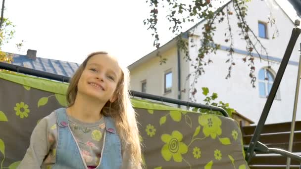 Petite fille blonde enfant s'amusant sur une balançoire en plein air pendant la journée ensoleillée d'été sur l'aire de jeux dans le jardin, concept d'enfance heureuse — Video