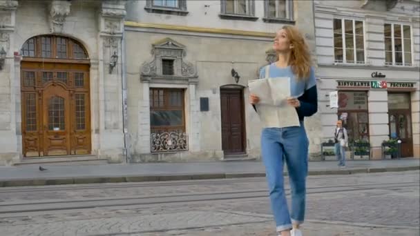 La mujer se pierde en la vieja ciudad europea mirando un mapa y buscando la dirección temprano en la mañana en la antigua plaza . — Vídeos de Stock