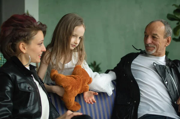 Retrato familiar de hija adulta, nieta pequeña y abuelo mayor en habitación loft con plantas de interior. Hombre y mujer están usando chaquetas de cuero negro en estilo punk, concepto de generación —  Fotos de Stock