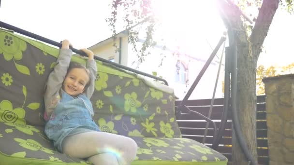 Niña pequeña rubia divirtiéndose en un columpio al aire libre durante el día soleado de verano en el patio de recreo en el jardín, concepto de infancia feliz — Vídeo de stock