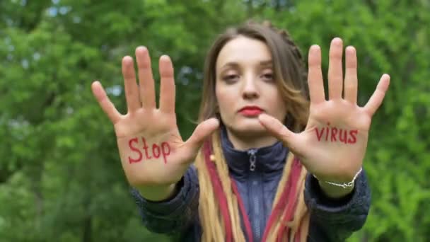 Nowoczesna poważna dziewczyna z długimi dredami pokazuje ręce z napisanym hasłem Stop wirusa na zielonym tle drzewa. Odpowiedzialność, koncepcje epidemii koronawirusów — Wideo stockowe