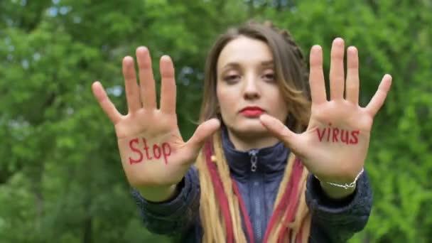 Modern seriös flicka med långa dreadlocks visar händerna med skriftlig slogan Stoppa virus på grönt träd bakgrund. Ansvar, koncept för epidemier av coronavirus — Stockvideo