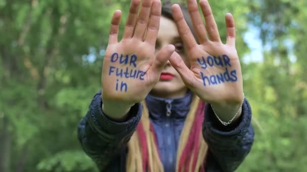 Chica seria moderna con rastas largas está mostrando las manos con el lema escrito Nuestro futuro en sus manos en el fondo del árbol verde. Responsabilidad, conceptos de cambio climático — Vídeo de stock