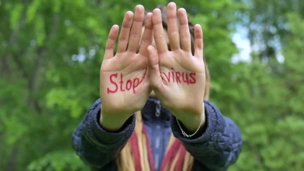 긴 레게를 가진 현대의 진지 한 여자 아이가 녹색 나무 배경에 Stop virus 라는 구호가 적힌 손을 보여 주고 있습니다. 책임감, 코로나 바이러스 유행하는 개념 — 비디오