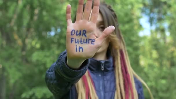 긴 레게를 가진 현대의 진지 한 아가씨가 녹색 나무 배경 위에 우리의 미래 라는 슬로건을 손에 들고 있습니다. 책임감, 기후 변화 개념 — 비디오