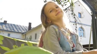 Küçük sarışın kız, yaz boyunca salıncakta sallanıyor güneşli bir günde bahçede oyun oynuyor, mutlu çocukluk konsepti.