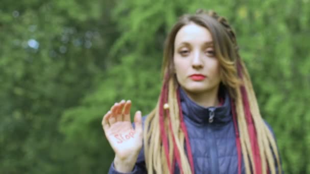 Modern seriös flicka med långa dreadlocks visar händerna med skriven slogan Stop på grönt träd bakgrund. Ansvar, klimatförändringar, protestkoncept — Stockvideo