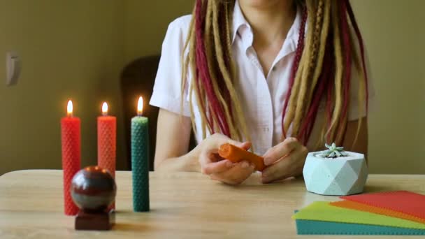 Giovane ragazza moderna con dreadlocks in camicia bianca sta eseguendo un workshop di fare candele di cera d'api seduto di fronte al tavolo con pietra e piante su di esso — Video Stock