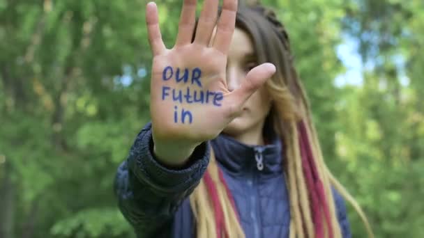 Modern seriös flicka med långa dreadlocks visar händerna med skriven slogan Vår framtid i händerna på gröna träd bakgrund. Ansvar, klimatförändringsbegrepp — Stockvideo