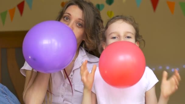 Kindergeburtstag. Kleine süße Mädchen feiert ihren B-Day mit junger Mutter mit Dreadlocks, die die bunten Luftballons auf Papiergirlanden zu Hause aufblasen — Stockvideo