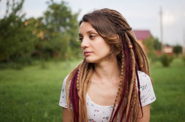 Gün batımında şehir parkında rastalı beyaz gömlek giyen modern bir kızın kadın portresi. Özgür ol, kendin ol.