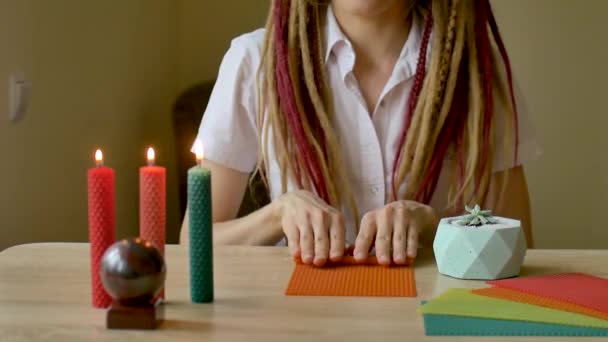 Молода сучасна дівчина з дредлоками в білій сорочці виконує майстерню з виготовлення бджолиних воскових свічок, що сидить перед столом з каменем і рослинами на ньому — стокове відео