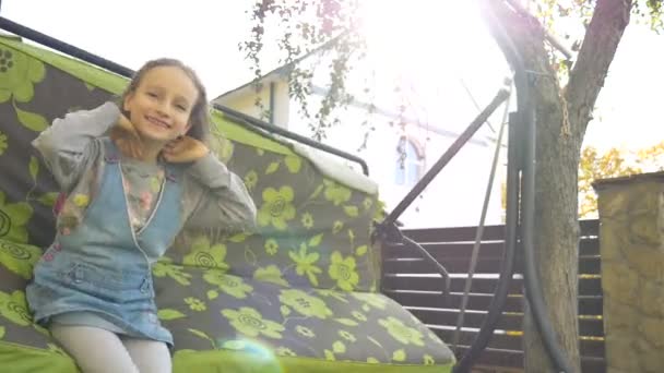 Kislány szőke lány szórakozás egy hinta szabadban nyáron napsütéses nap a játszótéren a kertben, boldog gyermekkori koncepció — Stock videók