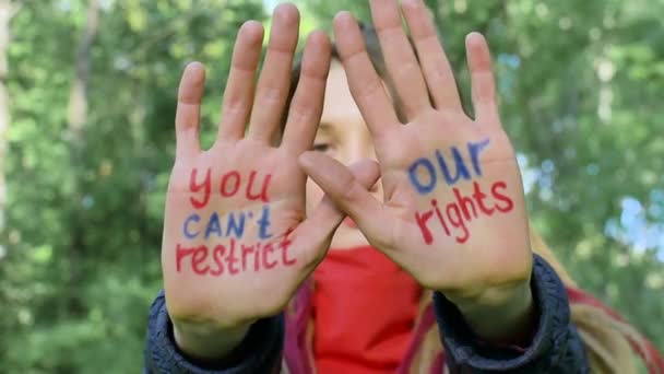 Moderna ragazza seria con lunghi dreadlocks in sciarpa rossa sta mostrando le mani con slogan scritto Non è possibile limitare i nostri diritti su sfondo albero verde. Responsabilità, concetti di protesta — Video Stock