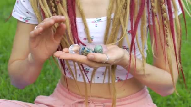 Menina com dreadlocks penteado segurando na mão pequenas pedras naturais rosa quartzo, strass, angelite, anyolite e azurite, rosto não é visível — Vídeo de Stock