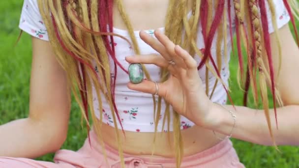 Портрет дівчини з дредлоками зачіска тримає в руці маленький натуральний камінь будьоліт — стокове відео
