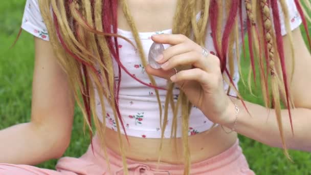 Ragazza adulta con lunghi dreadlocks sta tenendo trasparente viola uovo ametista yoni per vumfit, imbuilding o meditazione all'aperto sul suo sfondo del corpo all'aperto — Video Stock