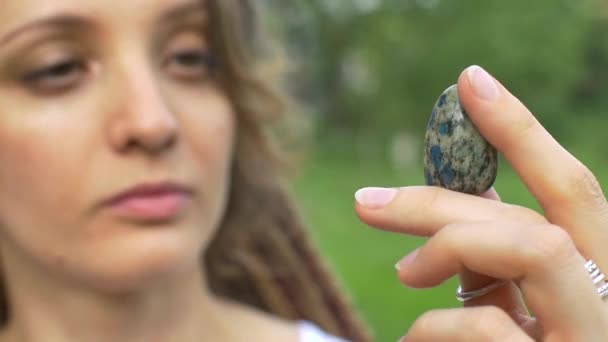 Młoda piękna dziewczyna z dredami trzyma w ręku azuryt, naturalny kamień na świeżym powietrzu w godzinach porannych w pobliżu jej twarzy z idealną skórą — Wideo stockowe