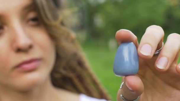 На відкритому повітрі портрет дівчини з дредлоками зачіска тримає в руці маленький натуральний кам'яний синій ангел — стокове відео
