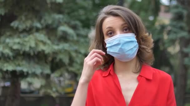 Молода жінка в червоній сорочці носить хірургічну маску на обличчі для захисту від вірусу під час пандемії. Коронавірус Ковід-19, карантинна концепція — стокове відео