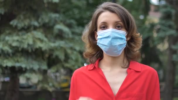 Mujer joven con camisa roja con máscara quirúrgica en la cara para protegerse del virus durante la pandemia. Brote de Coronavirus Covid-19, concepto de cuarentena — Vídeos de Stock