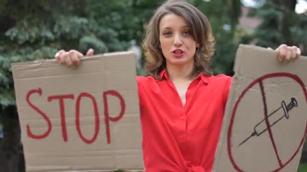 Jonge protesterende vrouw in rood shirt houdt protestbord plakbord met slogan Stop vaccin voor openbare demonstratie op bomen achtergrond. — Stockvideo