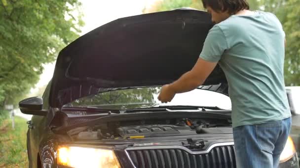 若い男が車のエンジンを見ている車の故障や道路上のエンジントラブルの間一人旅をしながら — ストック動画