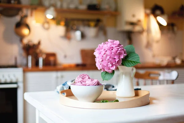 Pink cupcake and hydrangea flowers are serving on wooden tray. Morning breakfast on kitchen table.