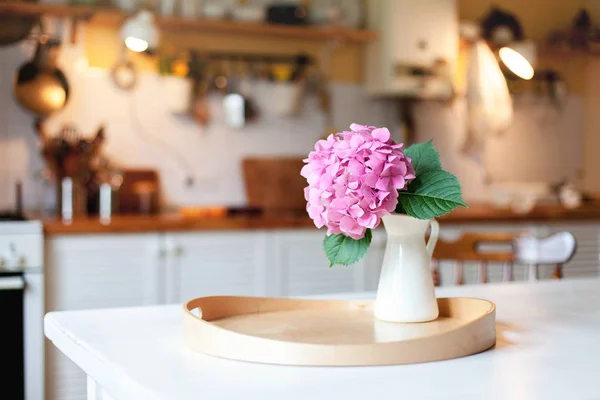 Pink hydrangea flower on wooden serving tray. Morning kitchen scene. Cozy home atmosphere hygge.