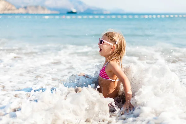 Kid is swimming in waves at sea beach in vacation. Child girl is enjoying summer holiday. Concept of travel, family fun and water safety. Lifestyle, authentic candid moments, emotions.