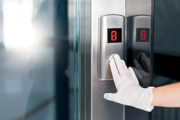 Female hands in medical protective gloves pressing elevator button.