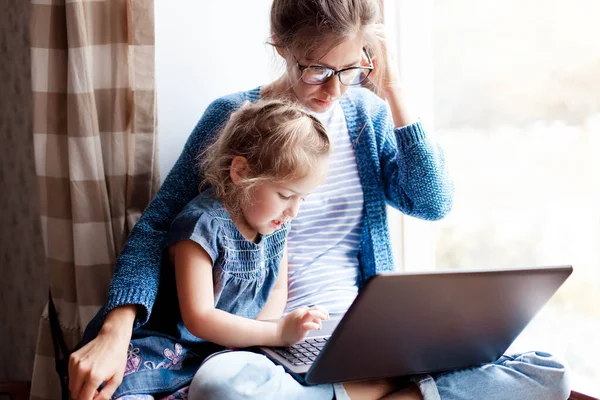 Working mom works from home office with kid. Mother and daughter read news. Woman and cute child