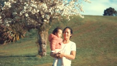 Asyalı Çinli kadın sakura ağaçları ile açık bir bahçede bebeğini taşıyan