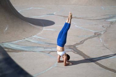 Following the trend of doing yoga in public spaces, Asian Chinese Woman does Yoga in public skate park clipart