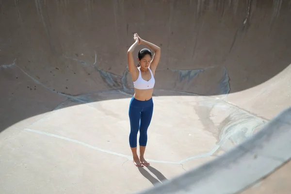 Following the trend of doing yoga in public spaces, Asian Chinese Woman does Yoga in public skate park